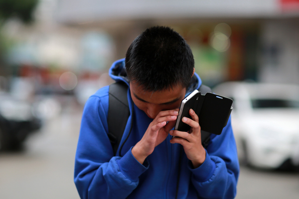 Jovem olha pra baixo com ouvido esquerdo próximo a aparelho celular. Foto: VCG (China Daily) 