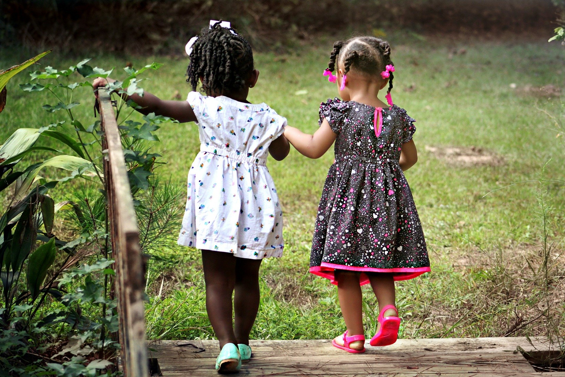duas menininhas negras de mãos dadas sobre uma ponte de madeira. Usam maria-chiquinha e vestidinhos